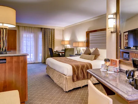 Guest room at Suites at Eden Resort, with a king bed, kitchenette counter with wet bar, wall-mounted TV, and a seating area by the balcony doors