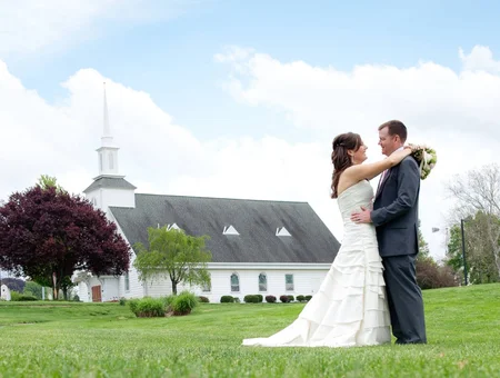 Bride and groom embracing on the lawn near DoubleTree Resort by Hilton Lancaster, with a white steeple chapel and mature trees behind them