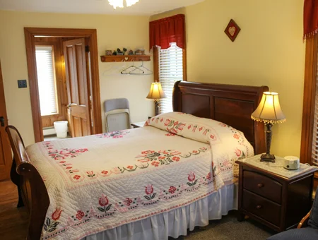 Bedroom with sleigh bed, embroidered floral quilt, and matching nightstand at Blue Rock Bed and Breakfast