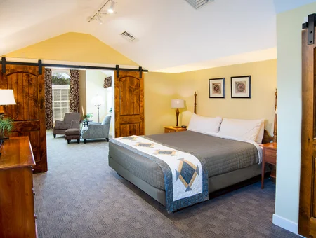 Bedroom with a quilted bedspread and sliding barn doors leading to a sitting area at Inn at Kitchen Kettle Village
