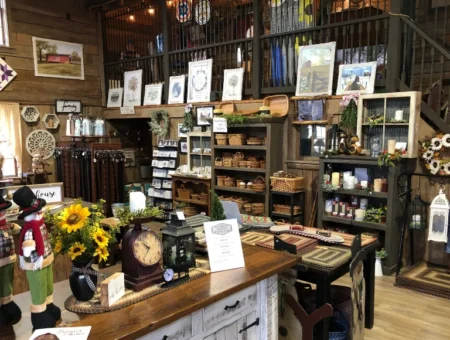 Store interior at Creative Rustic Furniture, with barn-style shelving displaying framed art, quilted decor, wicker baskets, and holiday accents around a checkout counter