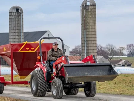 Farmer operating red compact tractor with front loader near grain silos from Farmco Manufacturing in Lancaster PA