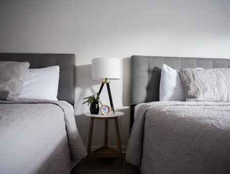 Two upholstered beds with a tripod lamp and side table between them at Carriage House at Strasburg