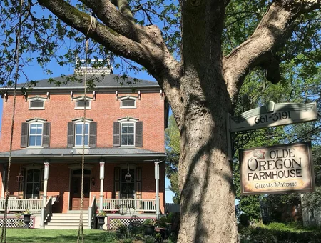 Olde Oregon Farmhouse exterior image: brick farmhouse with wraparound porch and Olde Oregon Farmhouse sign in Lancaster, PA
