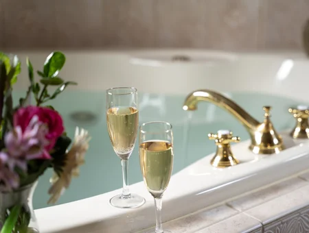 Champagne glasses and flowers beside a whirlpool tub with gold fixtures at Inn and Spa at Leola Village