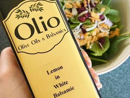 Bottle of Olio Lemon in White Balsamic held next to a spinach salad with cranberries