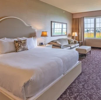 Hotel room with king bed, sitting area, and farmland view through large windows at AmishView Inn and Suites