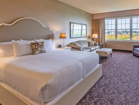 Hotel room with king bed, sitting area, and farmland view through large windows at AmishView Inn and Suites