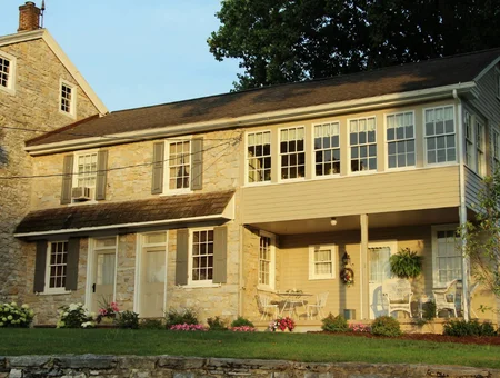Stone farmhouse with white porch and hanging flower baskets at Meadow View K Farm Guest House
