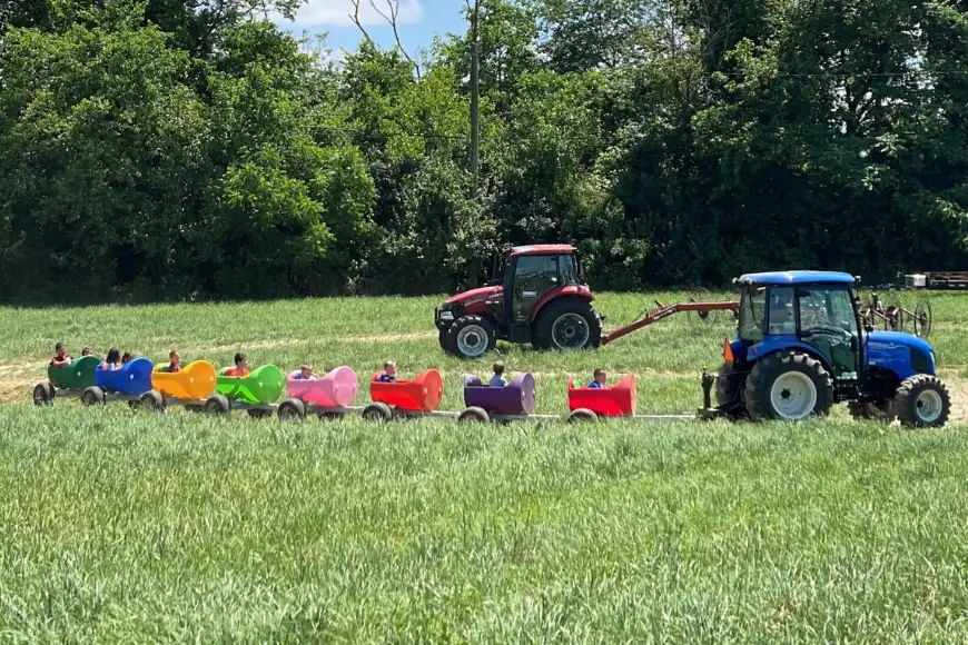 Tractor pulling colorful ride-on carts through a field on a farm field trip tour at Oregon Dairy Farmstead in Lancaster PA