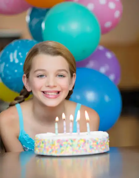 Young girl smiling in front of a birthday cake with candles and colorful balloons at a kids birthday party venue in Lancaster PA