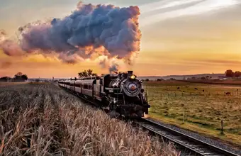 Historic steam train rolling through Lancaster County PA farmland at sunset