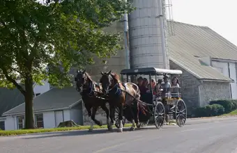 Amish horse-drawn buggy ride past a Lancaster County PA farm and silo