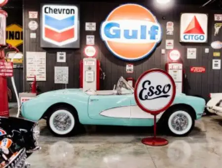 Vintage Corvette surrounded by classic Gulf Chevron and Esso gas station signs at Barry's Car Barn in Lancaster PA