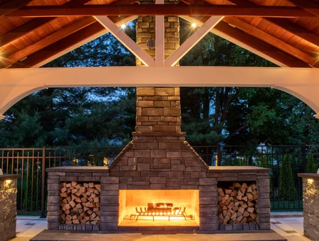 Clymer's Landscaping custom outdoor stone fireplace with wood storage under timber pavilion in Lancaster PA