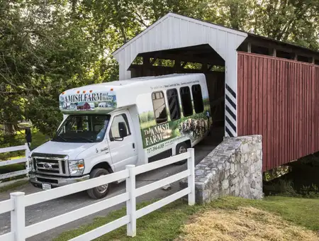 Amish Farm and House countryside tour bus passing historic covered bridge in Lancaster County PA