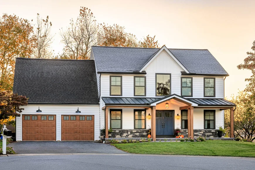 Modern farmhouse exterior with white board and batten siding, dark shingle roof, and wood garage doors by Eby Exteriors in Lancaster PA