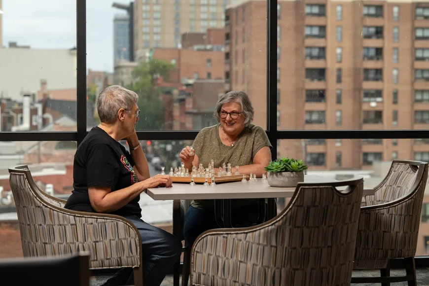 Landis Communities 55+ senior women playing chess at table with city view in Lancaster PA