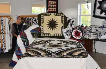 Amish quilter displaying black and white star pattern handmade quilt at Smuckers Quilts Lancaster County PA