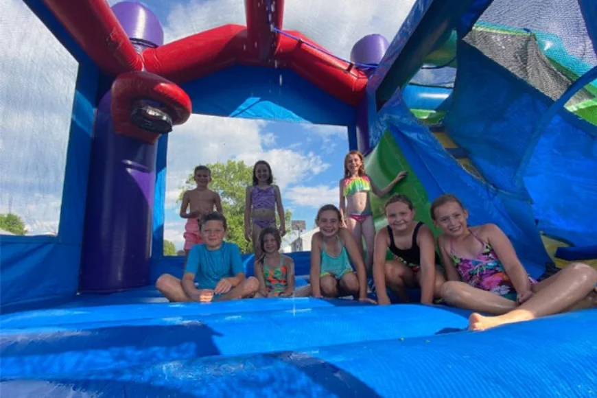 Group of kids in swimsuits posing on a water-slide bounce house rented from 3 Monkeys Inflatables