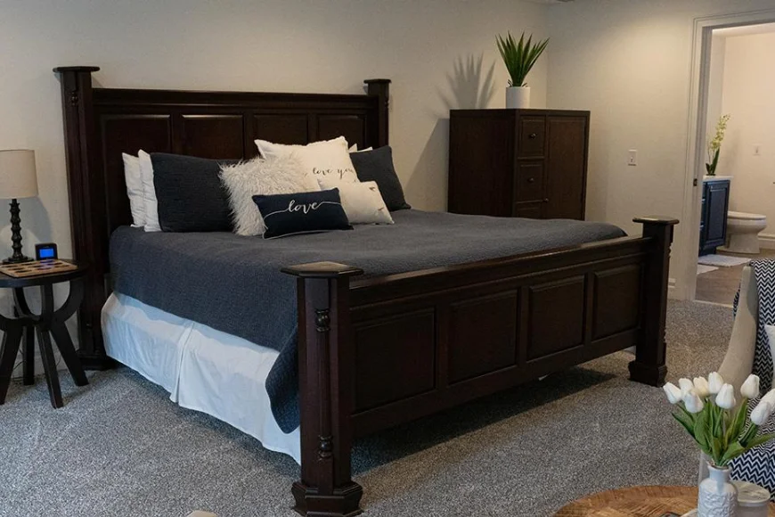The Barn at Strasburg B&B bedroom image: king bed with dark wood frame, navy and white throw pillows, and en suite bathroom in Lancaster, PA