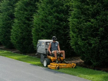 Landscaper on stand-on mower trimming grass along a hedge lined driveway for B and M Property Service in Lancaster County PA