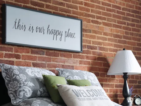 Bedroom with brick accent wall, decorative pillows, and a "this is our happy place" sign at The Courtyard Bed and Breakfast