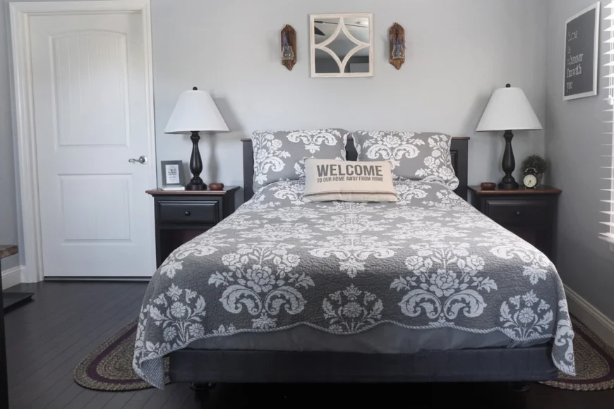 Bedroom with damask-patterned bedspread, twin nightstand lamps, and a "welcome" pillow at The Courtyard Bed and Breakfast