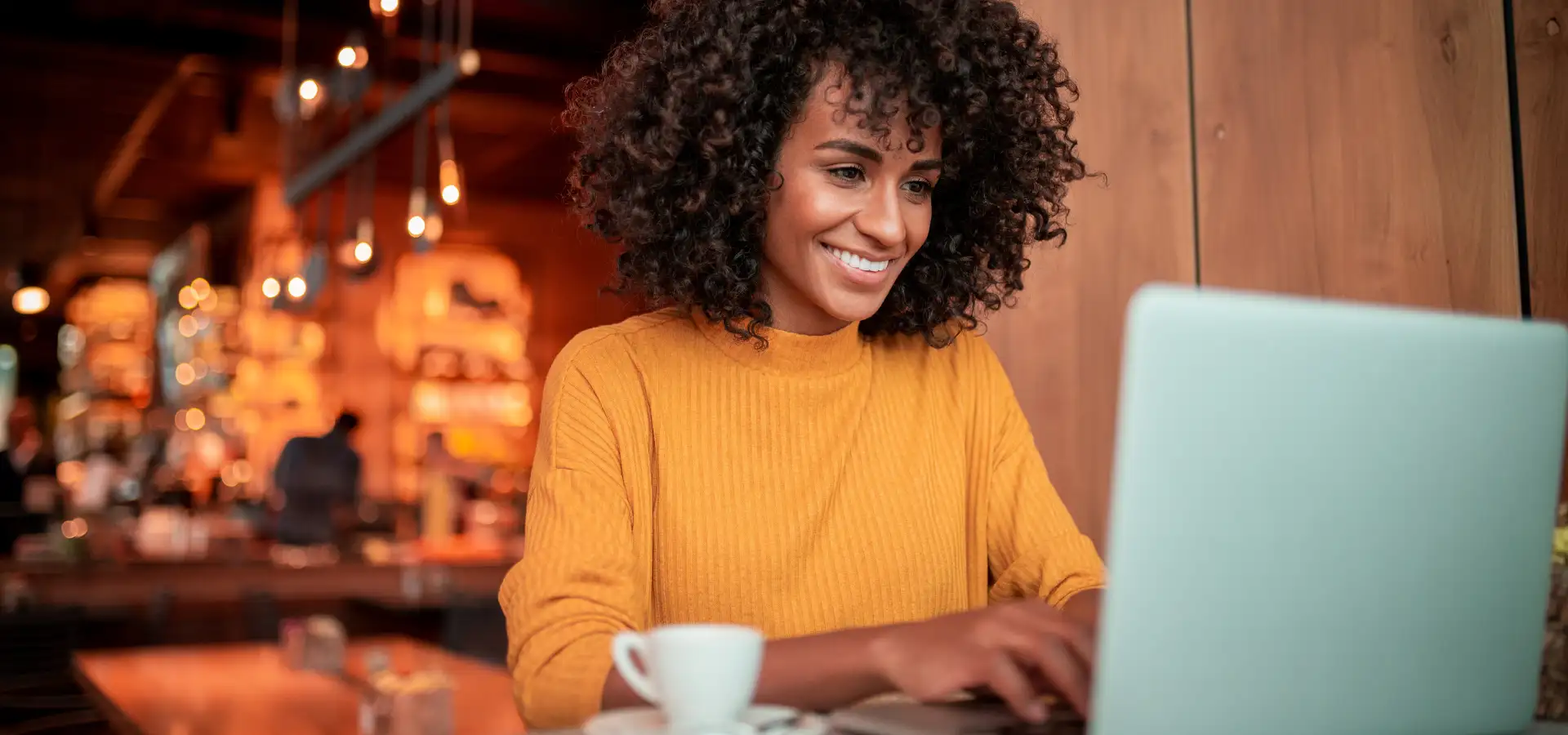 Woman shopping Cyber Monday deals online from a laptop at a Lancaster, PA coffee shop, smiling while browsing with a coffee cup nearby