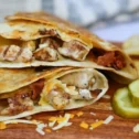 Grilled chicken quesadilla sliced in half at a Lancaster, PA deli, served with pickle slices and potato chips on a wooden board