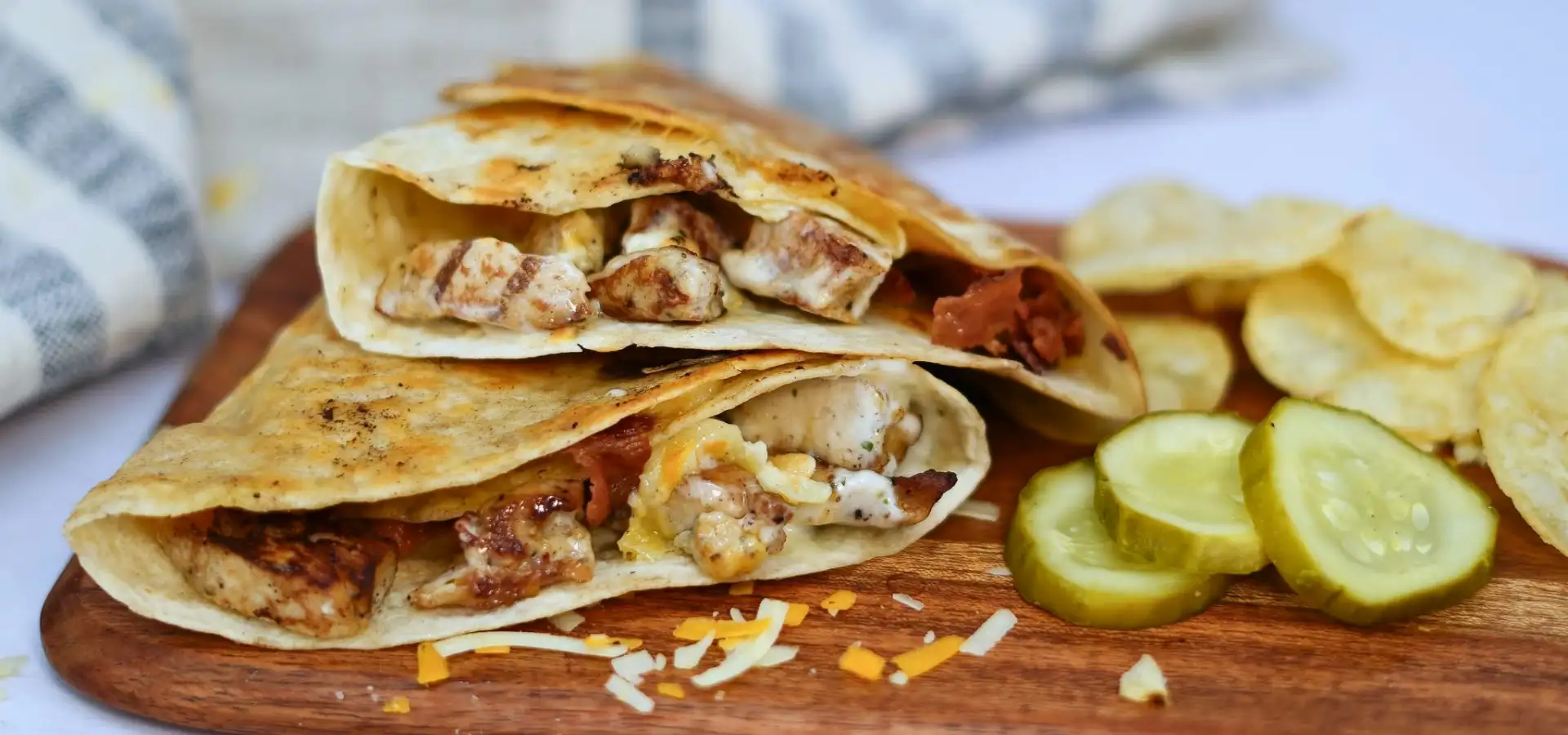 Grilled chicken quesadilla sliced in half at a Lancaster, PA deli, served with pickle slices and potato chips on a wooden board