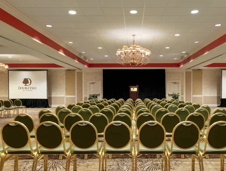 Rows of ballroom seating for a conference at DoubleTree Resort by Hilton Lancaster, facing a stage with a podium and projector screen under a chandelier