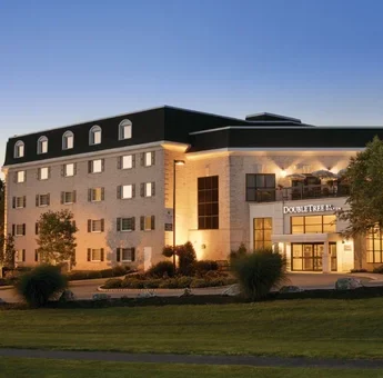 DoubleTree Resort by Hilton Lancaster exterior at dusk, with illuminated windows, a landscaped entrance, and a rooftop patio area lit above the main entrance