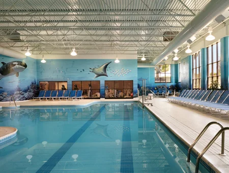 Indoor pool at DoubleTree Resort by Hilton Lancaster, with an ocean-themed mural, blue lounge chairs, and skylight windows along the wall