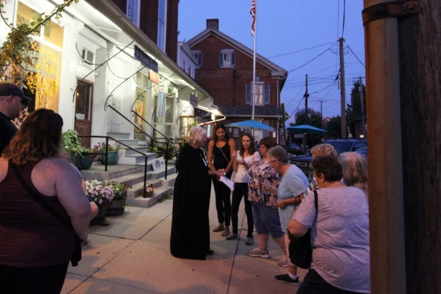 Cloaked tour guide leading visitors on a dusk street walk in Lancaster PA