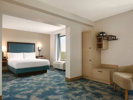Guest room at Hampton Inn Lancaster, with a teal upholstered headboard, patterned blue carpet, wardrobe cabinet, and a window seating area