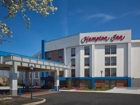 Hampton Inn Lancaster exterior on a sunny day, with a blue and white facade, covered entrance canopy, and blooming tree branches in the foreground