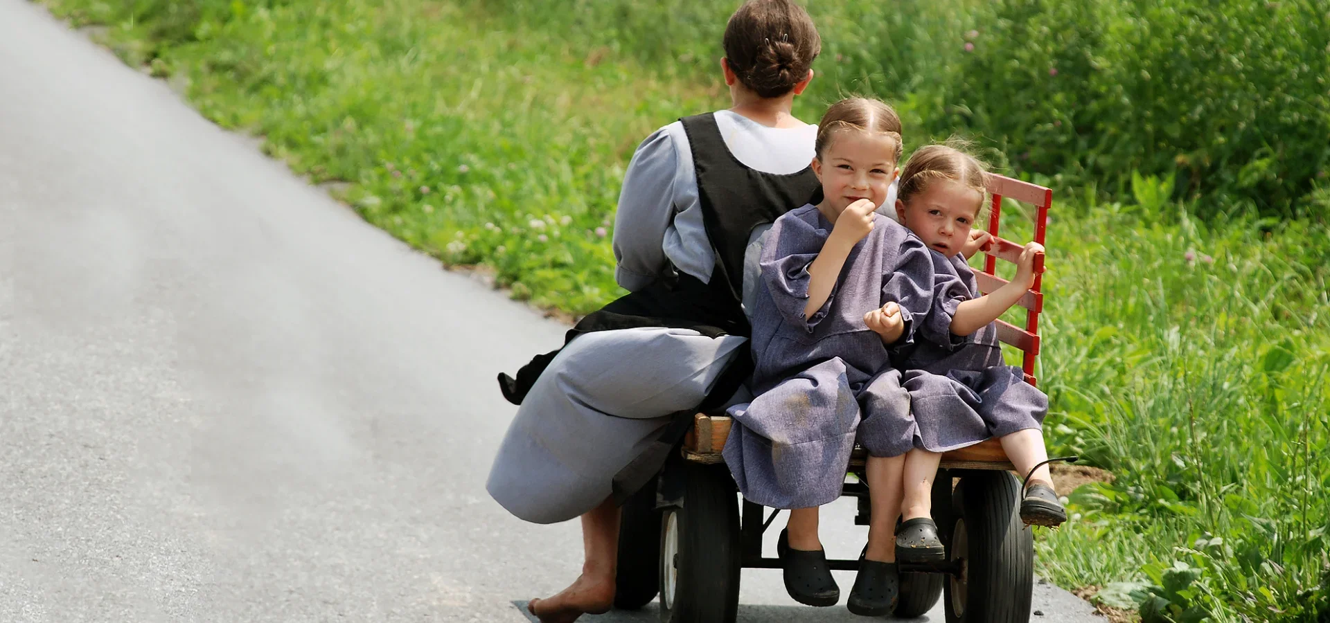 Amish children riding on a wagon along a country road, home page hero image for LancasterPA.com