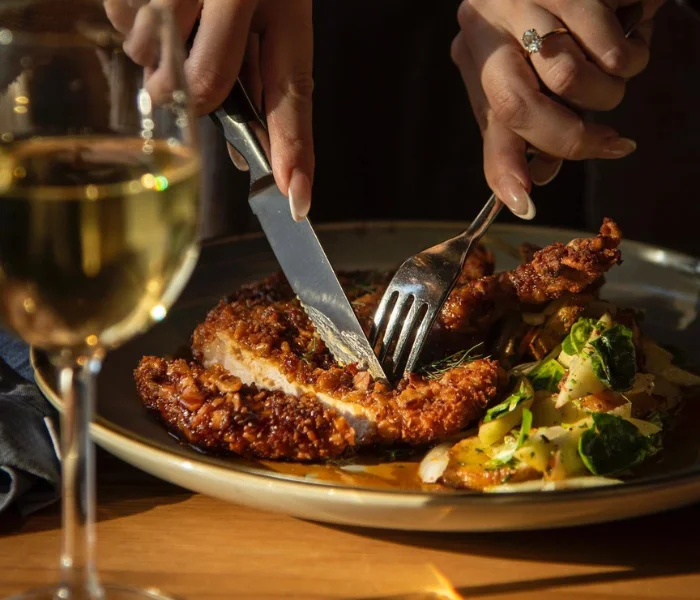 Diner cutting a breaded cutlet with a glass of white wine, home page hero image for LancasterPA.com restaurants