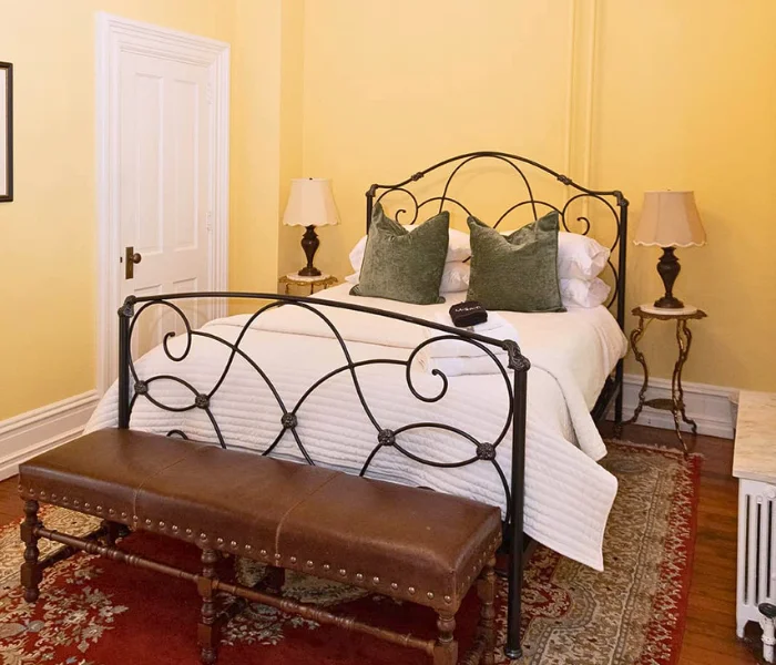 Wrought iron bed with green velvet pillows and a leather bench in a bedroom, home page hero image for LancasterPA.com shopping