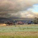 Amish farmers baling hay with a horse-drawn team near Intercourse, PA, under a dramatic storm sky at sunset