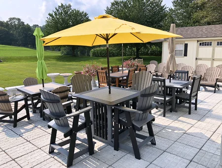 Outdoor patio set with poly Adirondack chairs, tables, and yellow umbrella on stone pavers