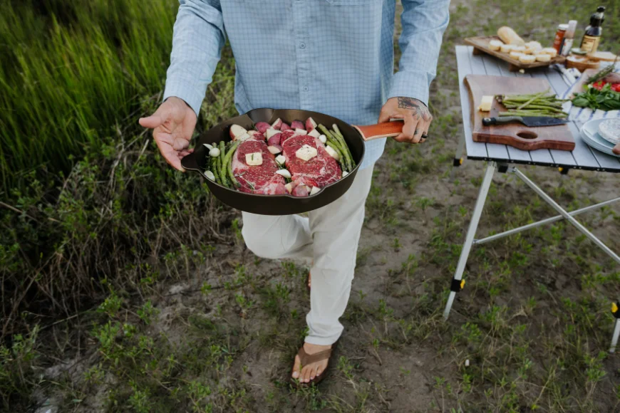 Man carrying steaks and asparagus in a Lancaster Cast Iron skillet outdoors made in Pennsylvania