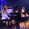 Musicians performing a candlelit piano and cello duet on stage at Prima Theatre in downtown Lancaster, PA, surrounded by rows of glowing candles