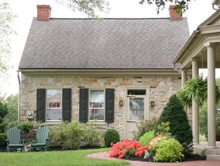Landis Farm Guest House stone farmhouse exterior, with a covered front porch, dark shutters, and landscaped garden beds along the walkway