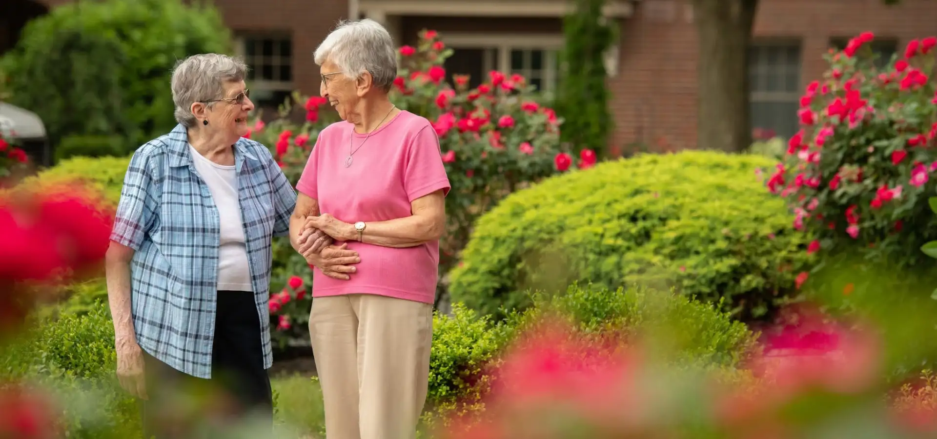 Two senior women arm in arm walking through rose garden at Landis Communities in Lancaster PA
