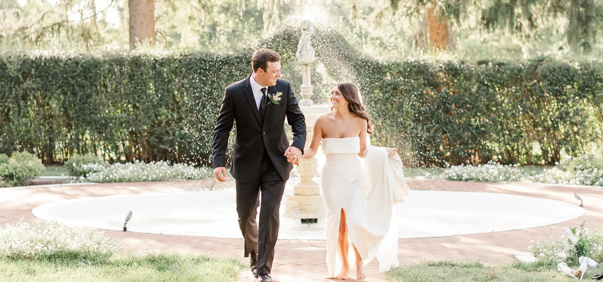 Bride and groom walking hand in hand past garden fountain at White Chimney wedding venue in Lancaster PA