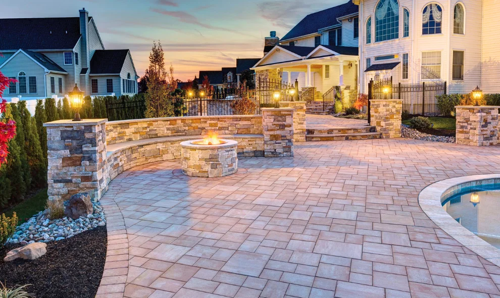 Backyard patio with stone fire pit, seat wall, and pool overlooking house at dusk, Lancaster PA landscaping