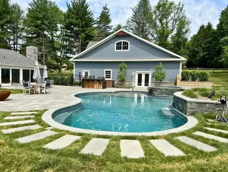 Kidney shaped pool with stepping stones and barn style home by Conestoga Buildings in Lancaster PA