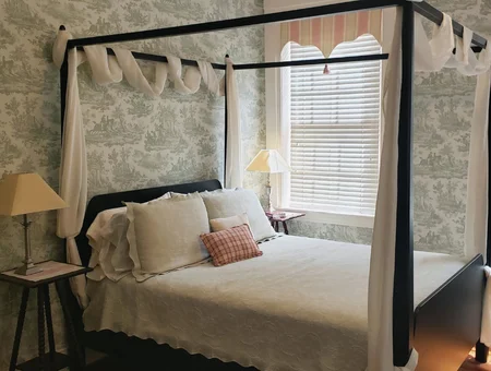 Canopy bed guest room at Rocky Springs Bed and Breakfast, with toile wallpaper, white linens, and a window seat with a lamp